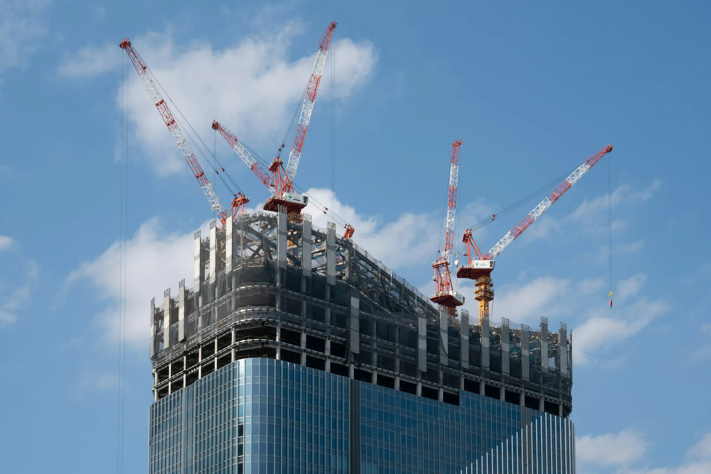 A supertall tower under construction, ringed by tower cranes against a bright sky