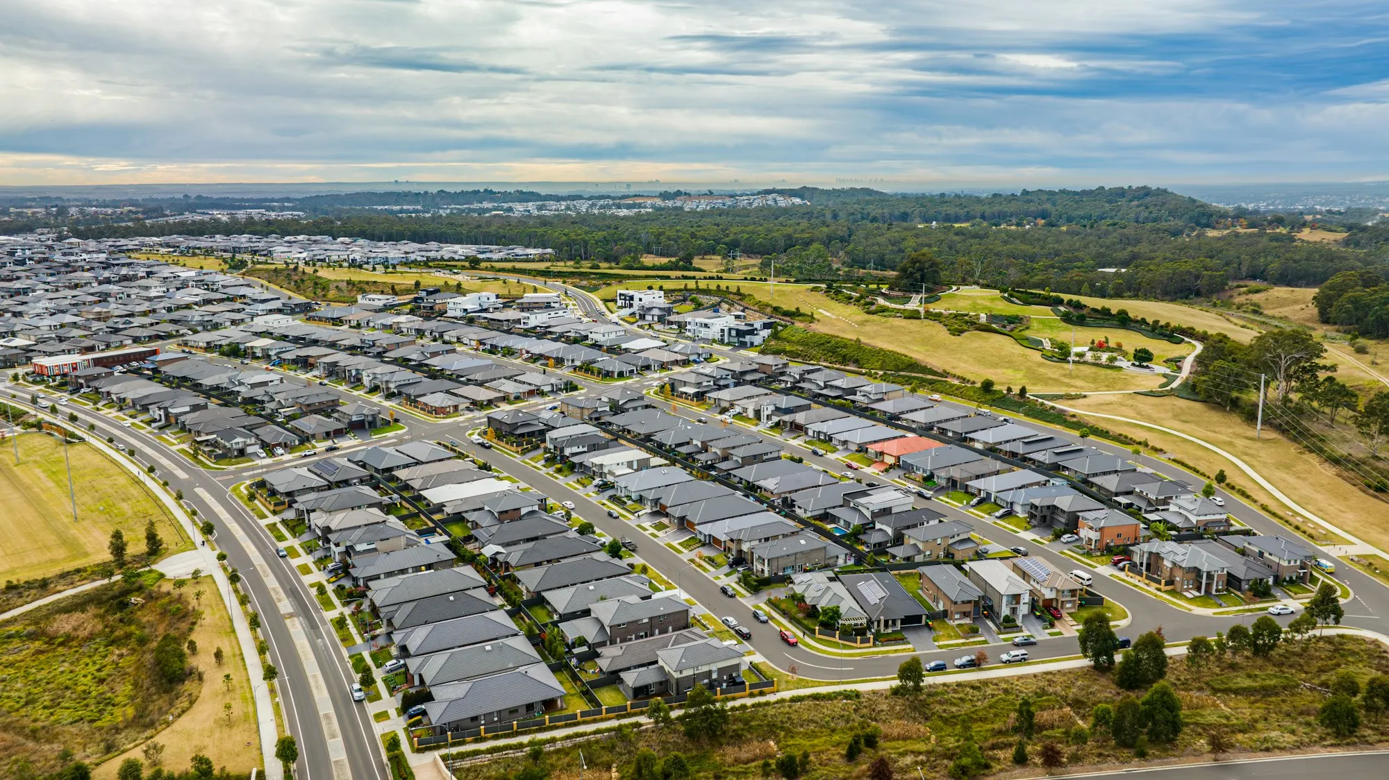 Aerial view of a newly built suburban housing estate, rows of pitched-roof homes cutting across green land